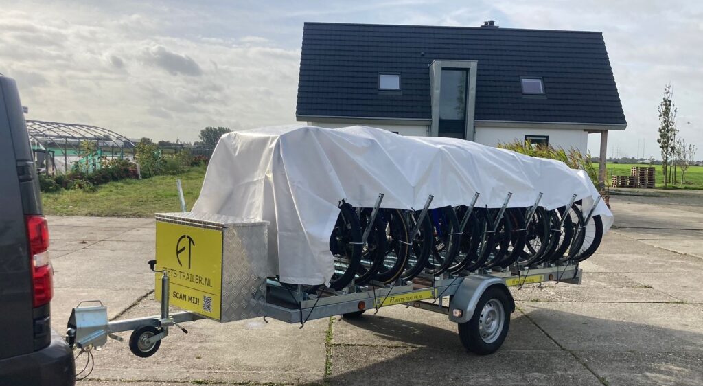 Een volle trailer met de beschermhoes over de fietsen heen.